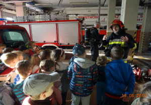 Dzieci rozmawiają ze strażakiem. W tle wozy strażackie.